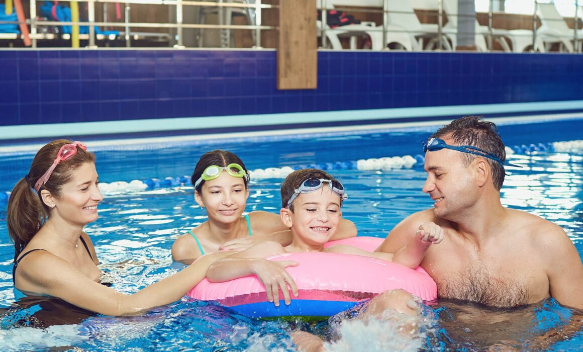 A photo of a mother, father and their two children (one girl and one boy) enjoying a swimming session.