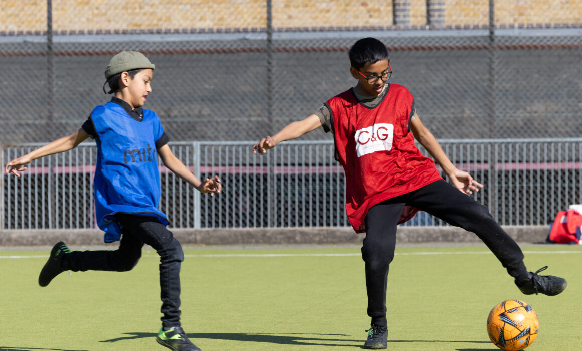 2 boys play football on a pitch