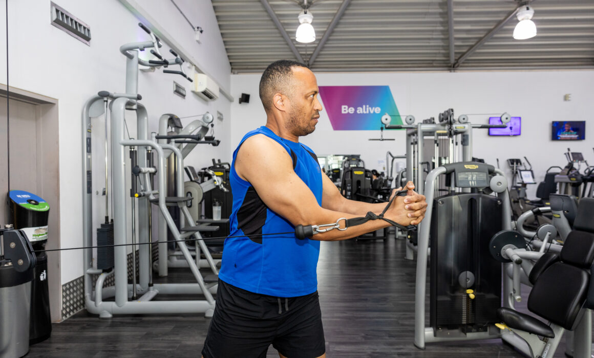 A photo of a man performing an arm exercise on a cable machine in a gym