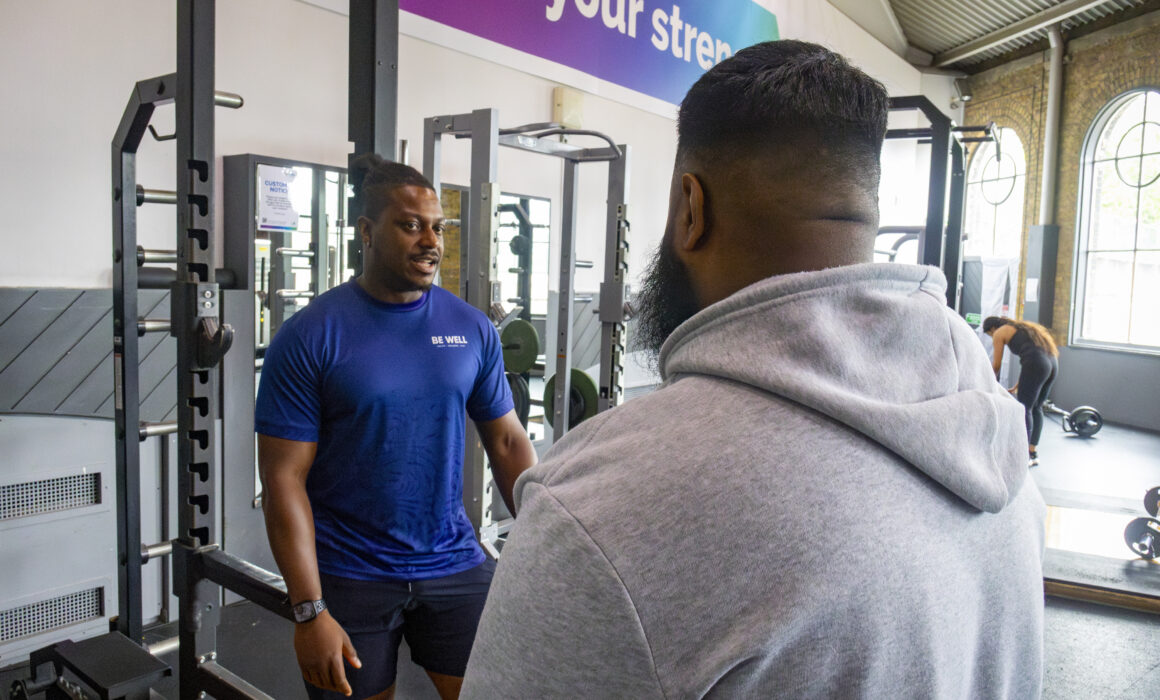A Be Well male staff member helps a male member in the gym