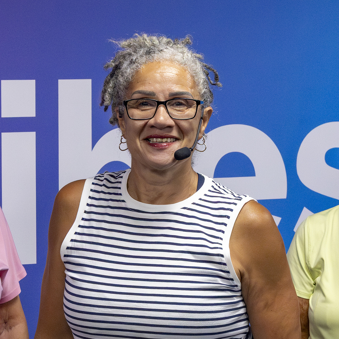 A photo of Be Well Health and Fitness Manager Wendy. She smiles whilst wearing a headset to teach a fitness class