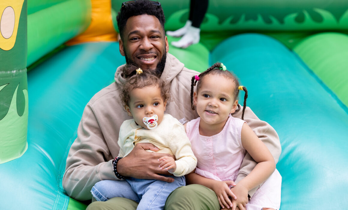 A photo of a man with his two young daughters smiling on a green bouncy castle